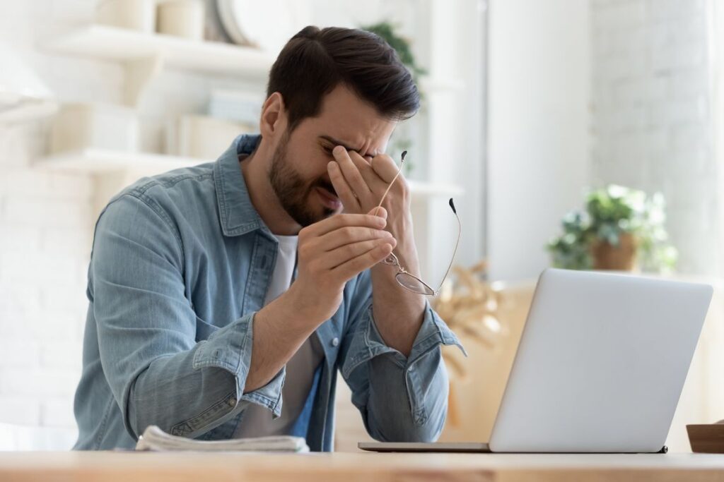 Person sitting at a desk, resting their head in their hands, looking exhausted and overwhelmed, with a glass of water and scattered papers around, symbolizing the struggle with fatigue.